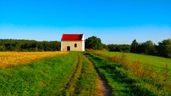 Grass road to chapel in beautiful European countryside during Summer morning.