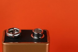closeup of a 9-volt battery's positive and negative terminals with a bold orange background
