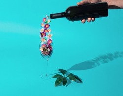Spring is poured. Horizontal flat lay compsition on a pastel cyan basground with male hand, wine bottle. glass and flowers. Minimal spring celebration concept