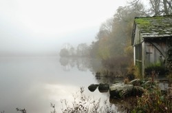Old disused wooden boat house on the lake side at Lake Grasmere in the Lake District on a misty autumnal morning 