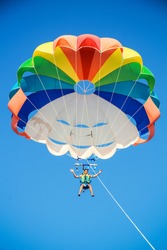 a young man in shorts is flying on a parachute on the blue sky background