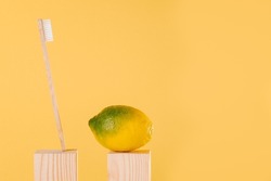 green and yellow lemon and bamboo toothbrush on light wooden podium on yellow background. Balance in oral health with natural eco-friendly ingredients and recycled products. Anti-gravity creative
