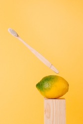 green and yellow lemon and bamboo toothbrush on light wooden podium on yellow background. Balance in oral health with natural eco-friendly ingredients and recycled products. Anti-gravity creative