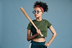 Im dangerous. Waist up portrait view of the multiracial woman wearing sunglasses holding baseball bat and feeling brutal while looking away. Self-defense concept