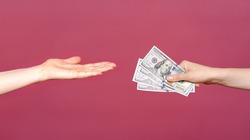 The woman reached a hand to take money isolated on a pink background. Palm up