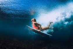 Surfer woman with surfboard dive underwater
