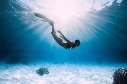 Young woman free diver glides over sandy sea with fins. Freediving in blue ocean