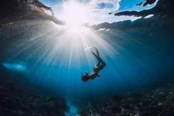 Free diver woman with fins over coral bottom and amazing sun rays. Freediving underwater in ocean