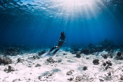 Freediver woman in bikini with fins glides underwater in tropical blue ocean
