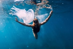 Woman underwater with jellyfish in blue ocean. Lady glides underwater in transparent sea