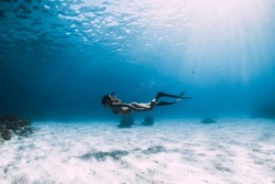 Attractive woman freediver with fins glides over sandy bottom. Freediving in blue ocean and sun rays