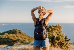 Woman with backpack outdoor and sunset light. Traveler girl walking in the mountains at ocean coastline