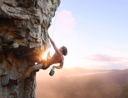 Young man climbing vertical wall with belay with sunrise valley on the background