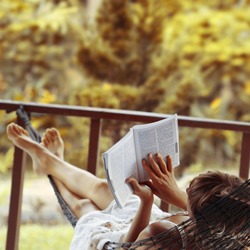 Woman lying in a hammock in a garden and enjoying a book reading