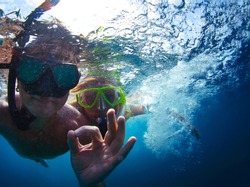 Young active couple snorkeling in a sea and giving ok signal