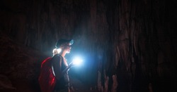 Young woman with backpack explores the cave with the torch
