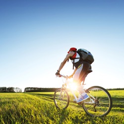 Young man cycling on a rural road through green spring meadow during sunset
