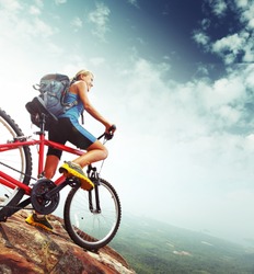 Female tourist with backpack and bicycle enjoying valley view from top of a mountain