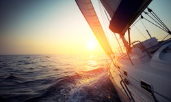 Sail boat gliding in open sea at sunset