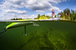 Split shot of the man fishing from the boat on the lake. Underwater view of the lake. Focus on the bait