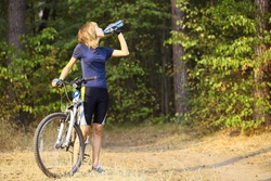 Young woman with bike drinking water from bottle