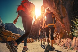 Hikers with backpacks walk on the trail in canyon of Zion National Park, USA