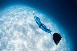 Woman freediver glides over sandy sea bottom with monofin