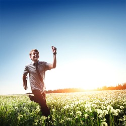 Happy young man with laptop in hand running on meadow with dandelions
