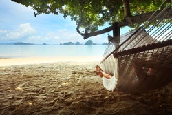 Woman lying in a hammock in tree's shadow on a beach