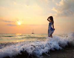 Woman in summer dress standing on a sea coast and looking to the horizon