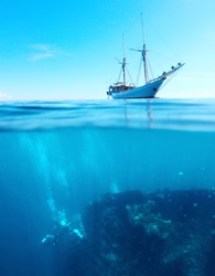 Sail boat in a tropical calm sea on a surface and divers underwater exploring a shipwreck