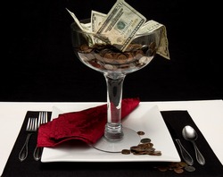 Money in large serving dish sitting  on top of dinner plate being served as though it were a dessert.