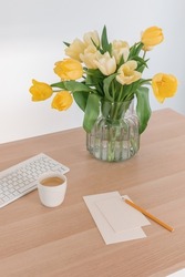 Blank paper cards mock up, cappuccino, keyboard, beautiful bunch of flowers in vase on table. Inspiring workplace.