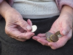 Old wrinkled hands hold a coin. Pensioners count pennies, living wage, poverty and survival. Basic income below the poverty line. Economic problems of old people, lack of money.
