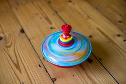 A colourful spinning top on a wooden floor spins round very fast so as to create motion blur. The red, yellow and blue colours blend together to create a watery appearance. 