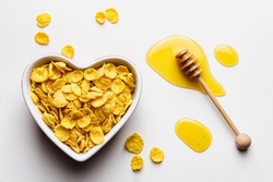 Corn flakes in heart bowl with honey on white background. Top view of healthy breakfast.