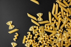 Different kinds of raw pasta with copy space on black background. Top view of Italian cuisine ingredient.