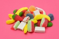 Pile of delicious colorful, tasty candies of different shapes on a pink background.