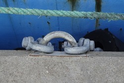 Close up of grey metallic mooring ring on dock on the stone pier. Blue damaged rope. Old blue painted metal with rust background.