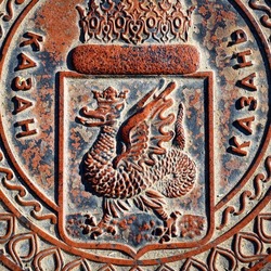 Dragon image on manhole cover in Kazan, Tatarstan, Russia. Sewer lid with coat of arms of Kazan close-up. Top view of metal manhole cap with traditional emblem and word Kazan in Russian and Tatar.