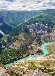 Sulak Canyon in Dagestan, Russia. Scenic vertical view of deep canyon, natural landmark of Caucasus. Panorama of mountains and blue green water, landscape of gorge with river and village in summer.