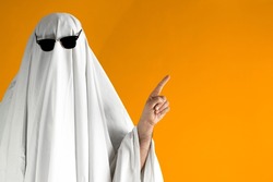 Person in Halloween costume of ghost with sunglasses points away