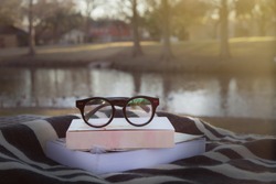 old fashioned eye glasses on books with black and white cloth and blurry lake background, filtered tone