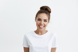 Joyful attractive european woman with stylish hairstyle showing tongue and smiling, being in good mood while standing against white background. Childish girlfriend won bet and now rejoicing