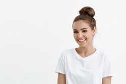 Fashionable cute european female with bun smiling broadly and glancing at camera while standing over white background. Stylish fitness trainer explains how to lose weight without harm for health