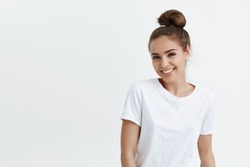 Charming adult caucasian woman with bun smiling broadly and glancing at camera, standing against white background. Cute wife on meeting with girlfriends. Girl in dressing room changes to her sportsuit