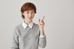 Friendship and emotions concept. Positive and attractive redhead girl with short hair and freckles, winking while smiling and showing victory or peace gesture, greeting friend or posing at camera.