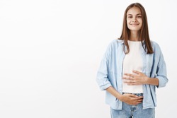 Sound mind in healthy body. Portrait of delighted joyful young european female taking care of health touching belly or stomach with pleased happy smile taking vitamins or drinking yoghurt