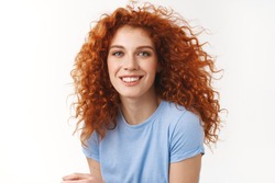 Close-up tender alluring redhead woman with curly hair that floats in air, smiling joyfully and coquettish gaze camera, enjoy summer ocean breeze, strands floating in air, stand white background