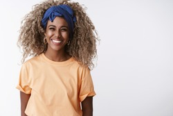 Waist-up shot friendly and sincere, attractive african-american blond girl with afro hairstyle, stylish headband and orange t-shirt, laughing and smiling joyful, have fun standing white background